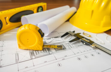 construction-plans-with-yellow-helmet-drawing-tools-bluep